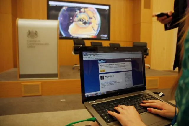 Woman typing on a laptop with a Foreign and Commonwealth Office Lectern in front of her and a large screen