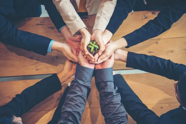 A group of hands holding soil and a seedling