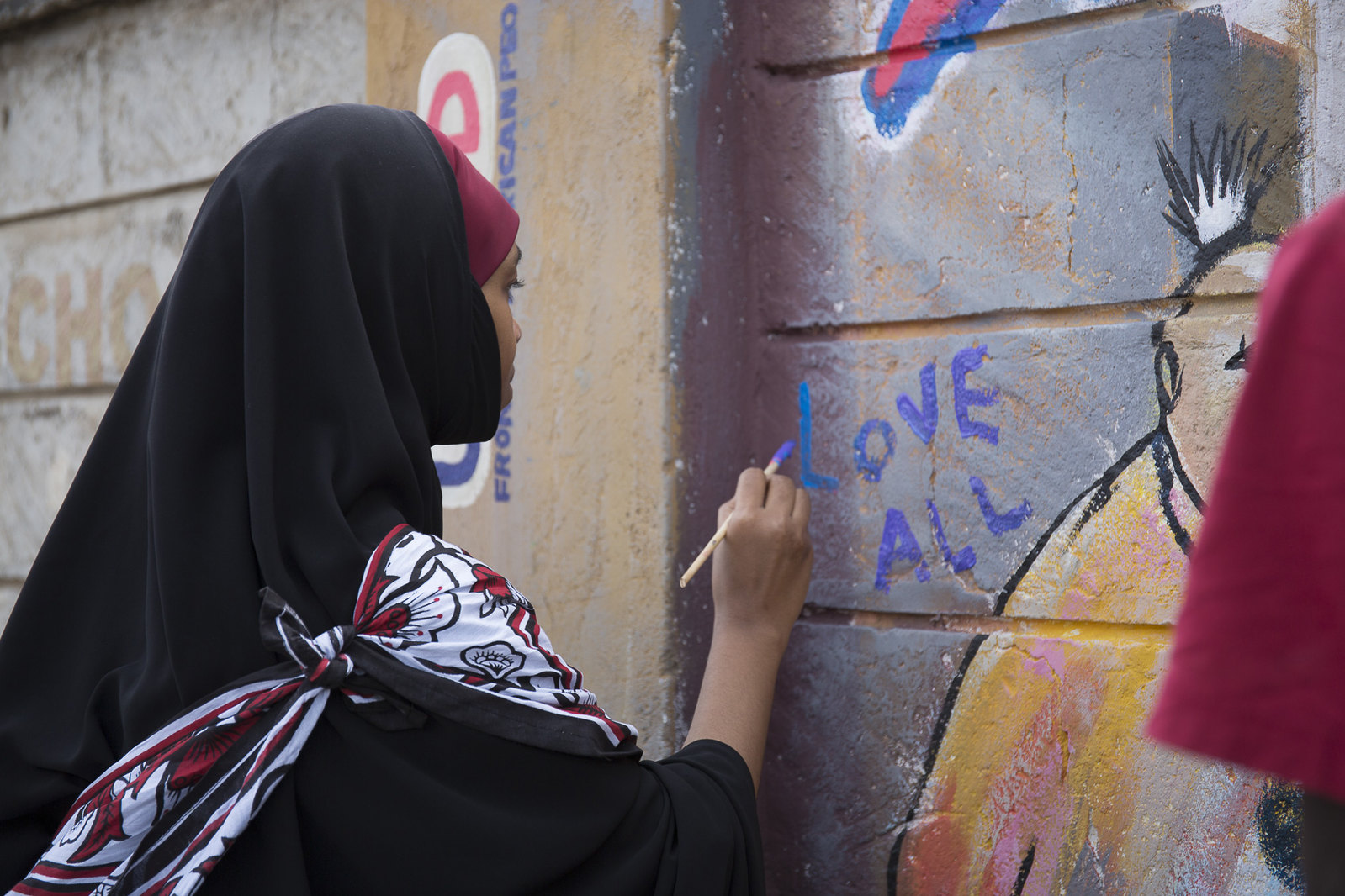 A young woman signs a peace mural during the USAID
