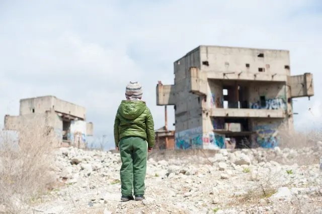 A child stands facing derelict buildings.