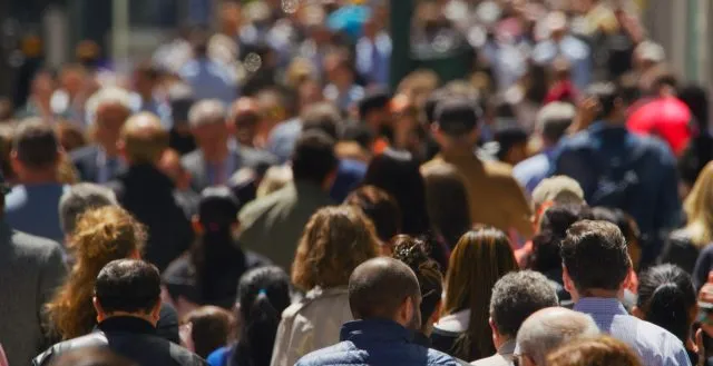 A crowd of people walking down a street are viewed from behind.