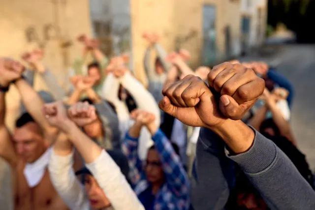 Protestors stand with their hands raised in the air.