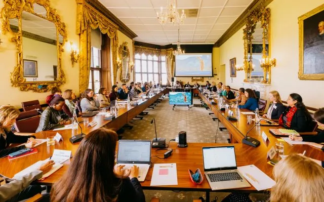 Wide view as participants sit around a large table at a Wilton Park Dialogue on Women's Economic Empowerment.