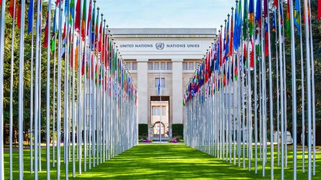 The United Nations Office in Geneva with flags of UN members leading up to the entrance.