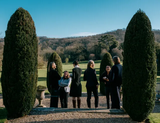 Guests at a Wilton Park event stand together in the gardens drinking tea.