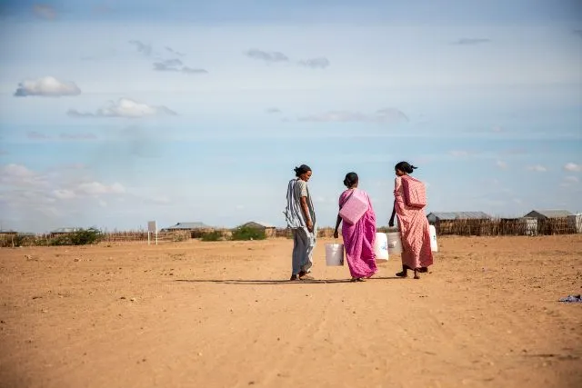 Image shows three people walking and carrying wash kits and large buckets.