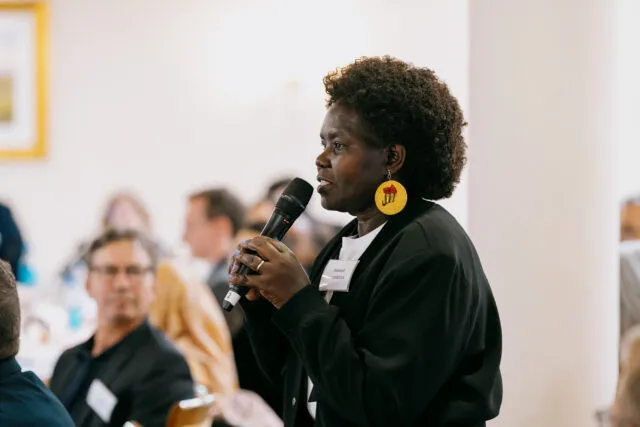Robinah Alambuya, Vice Chair of the African Disability Forum, holds a microphone as she addresses participants.