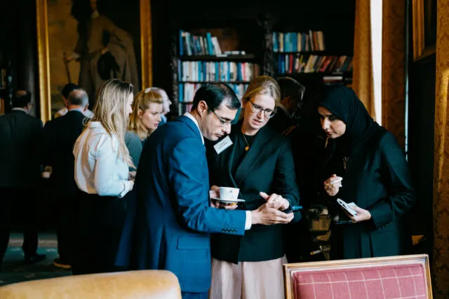 Three participants gather to look at something on a mobile phone, in the Wilton Park library