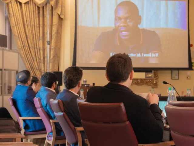 Participants in the conference room watch a screening of the film 'Lithium Rising: a race for critical minerals.'