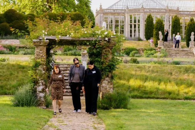 Three participants walk from beneath a rose arch