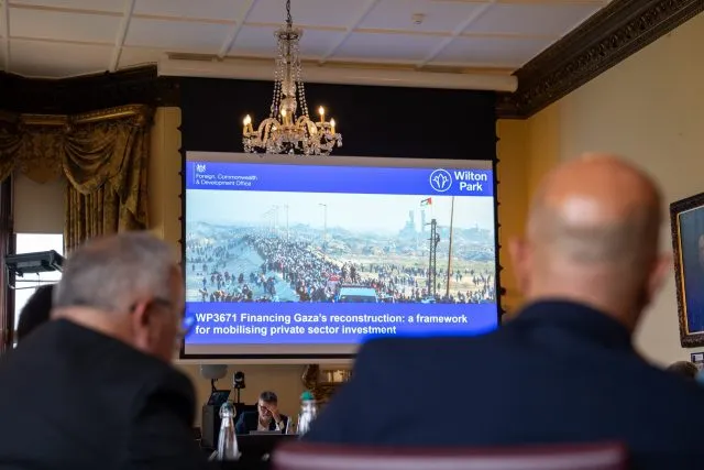 A large screen in the conference room displays an image of Palestinian people returning to their homes after the January 2025 ceasefire