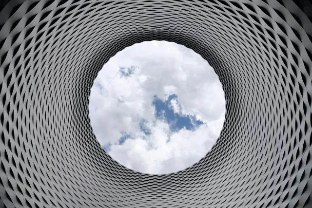 A circle of sky seen from within a latticed metal chimney