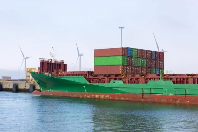 A cargo ship in harbour with wind turbines behind it
