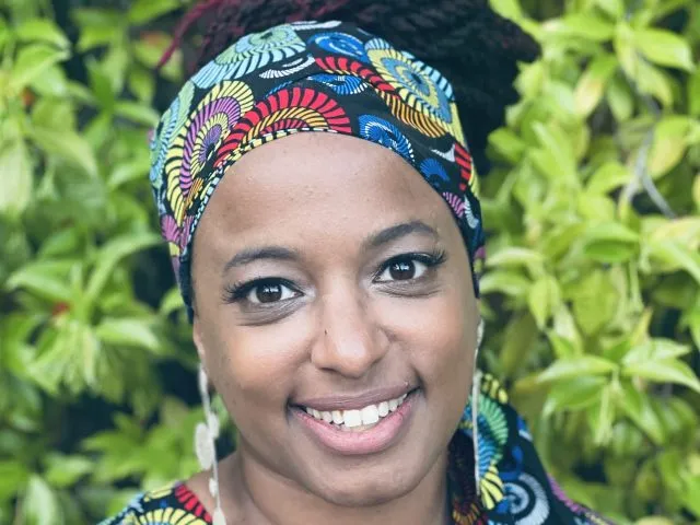 A headshot Astrid Haas smiling at the camera, wearing a brightly coloured headscarf.