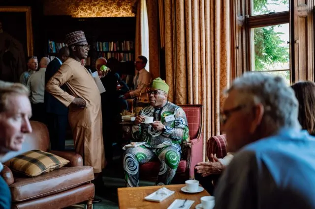 Participants sit and enjoy a cup of tea in the margins of an event. They sit on large armchairs in the Wilton Park library.