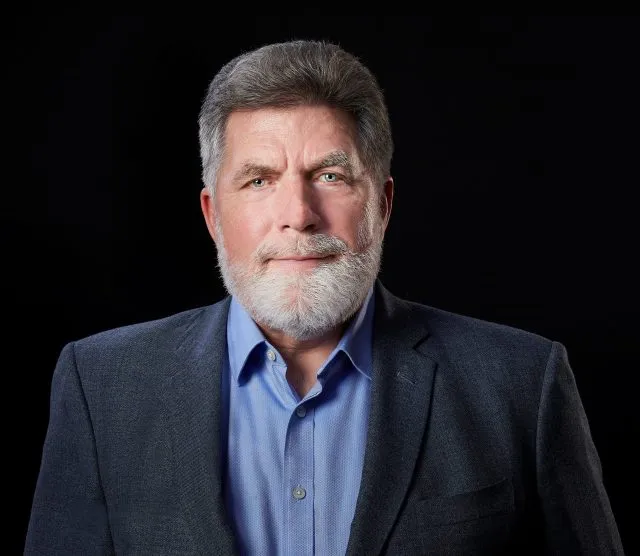 Dr Brad Roberts wearing an open necked blue shirt and jacket, looking directly at the camera.