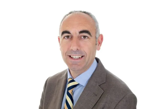 Rob Black, Associate Programme Director at Wilton Park, wearing a suit, blue shirt and striped tie. He is smiling and looking directly at the camera.