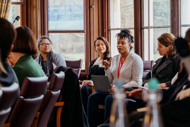 A participant speaks i the conference room, as she sits by a window