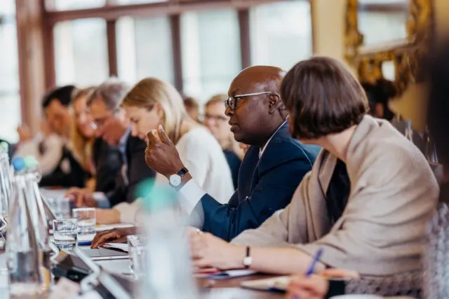 A participant raises his hand as he speaks at the conference table