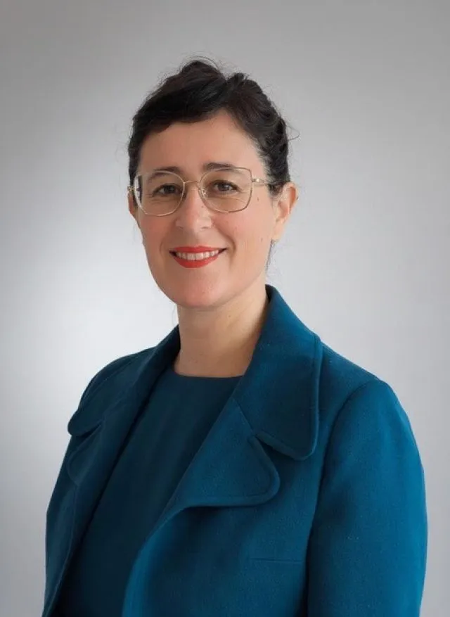 Dr Émilie Medeiros, Founder and Director of Manas, wearing a teal jacket is smiling and looking at the camera
