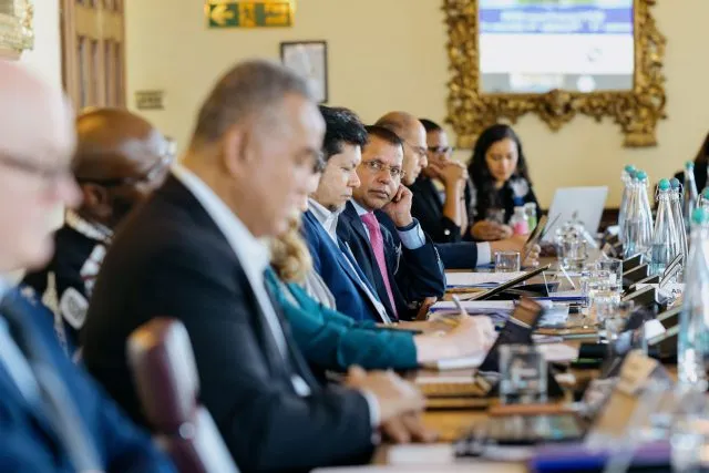An image showing a row of participants sitting and the conference table. The camera focuses on one panellist.