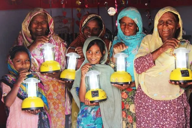 A group of women and girls wearing saris hold brightly lit solar lamps