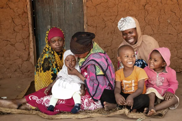 Kwale County, A woman is seated carrying a baby with her family at their homestead.