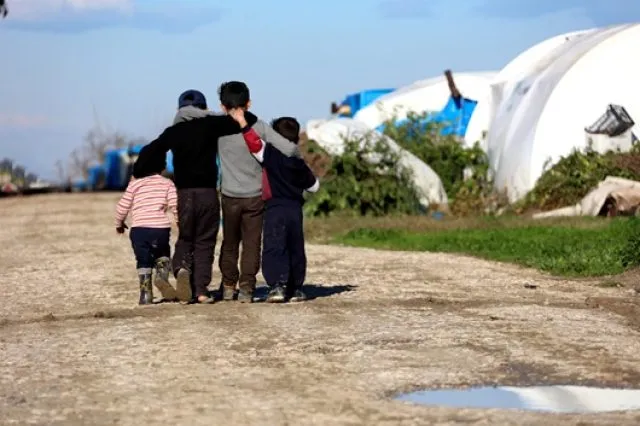 A group of Syrian children in a refugee camp stand with their arms around one another, facing away from one another.