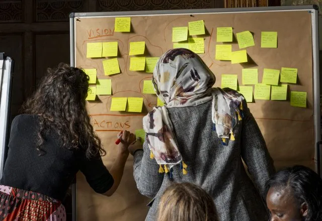 Two female participants add post-it-notes to a large corkboard