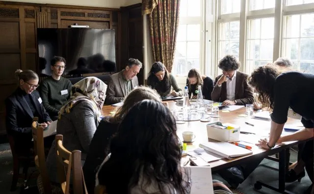Participants gathered round a table by large, light windows, taking part in a breakout group