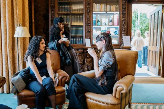 Three participants talk as two of them sit in armchairs and one leans on the back of a chair