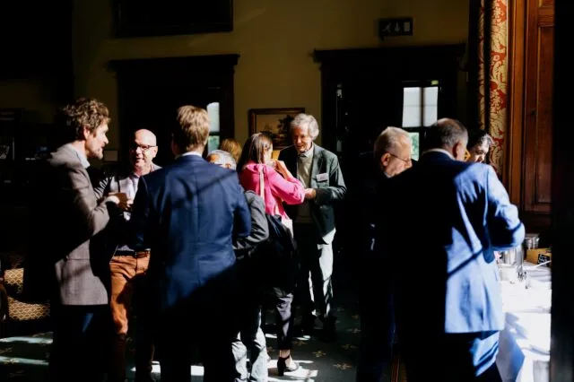 Participants talk during the tea break, standing in strong sunlight and shadow