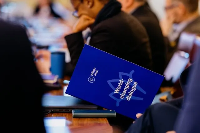 A participant holds a folder with Wilton Park branding on the front cover