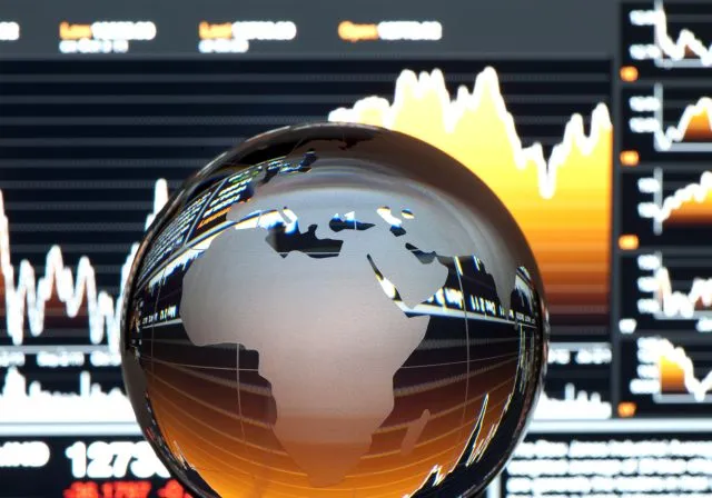 A glass ball depicting a globe, sits in front of a screen with financial data showing.