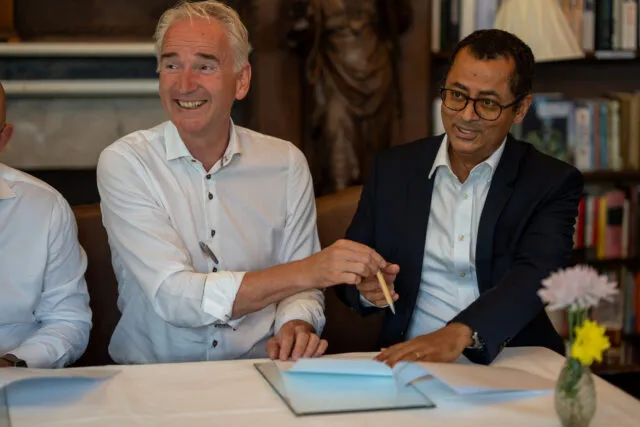 A man passes a pen to a colleague as they read through documents to sign