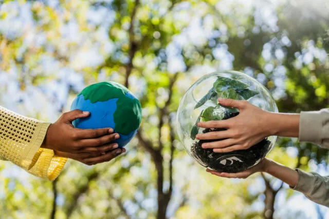 A close up of hands holding a globe and a sphere containing plants.