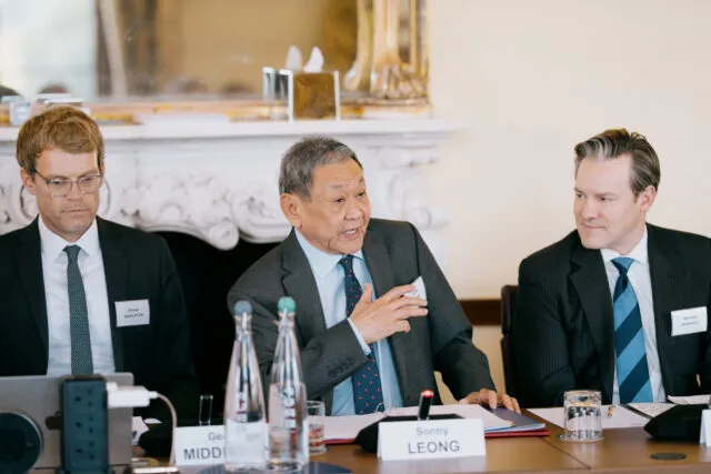 Minister Leong sits at a table, hand outstretched, as he delivers opening remarks at an event at Wilton Park.