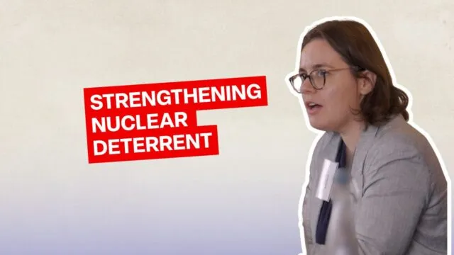 A participant seated at the conference table, wearing glasses and a light grey jacket. Large red and white text on the left reads “STRENGTHENING NUCLEAR DETERRENT”.